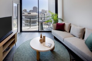 A modern living room with a large TV, a round coffee table, a sofa, and a balcony with a city view. - The Star Residences Gold Coast (Gold Coast)