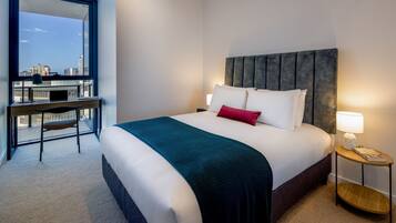 A hotel room with a bed, a desk, a chair, a nightstand, and a view of the city.