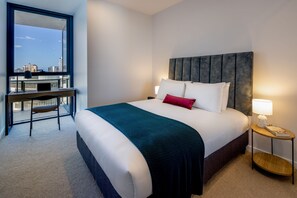 Habitación de hotel con cama, escritorio, silla, mesita de noche y vistas a la ciudad.