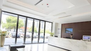 A modern hotel lobby with a reception desk, seating area, and large windows offering a view of the street. - City Convenient Zhuzhou Sports Centre (Zhuzhou)