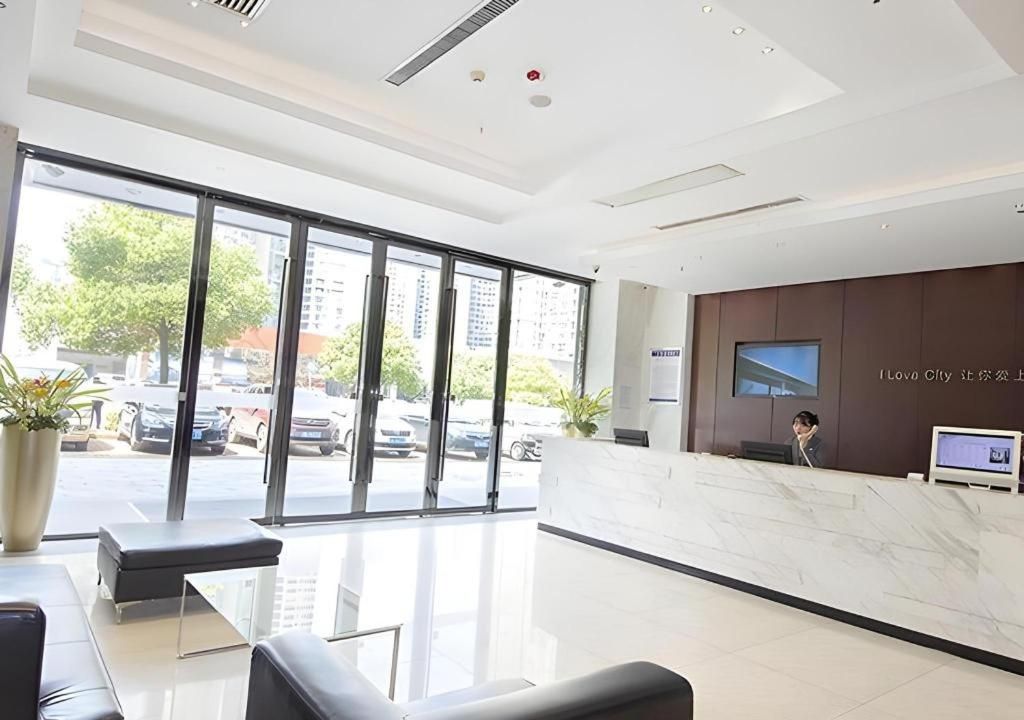 A modern hotel lobby with a reception desk, seating area, and large windows offering a view of the street.