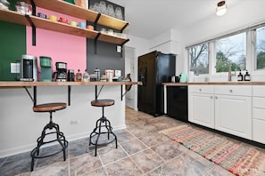 Una cocina moderna con un refrigerador negro, armarios blancos y una alfombra colorida.