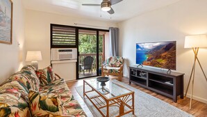 A living room with a sofa, coffee table, TV, and a ceiling fan. - Banyan Harbor #F71, Walk to Beach, Wifi, AC, Pool, Parking, Laundry (Lihue)