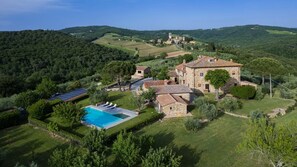 Una amplia villa de piedra con piscina, rodeada de exuberante vegetación y colinas.