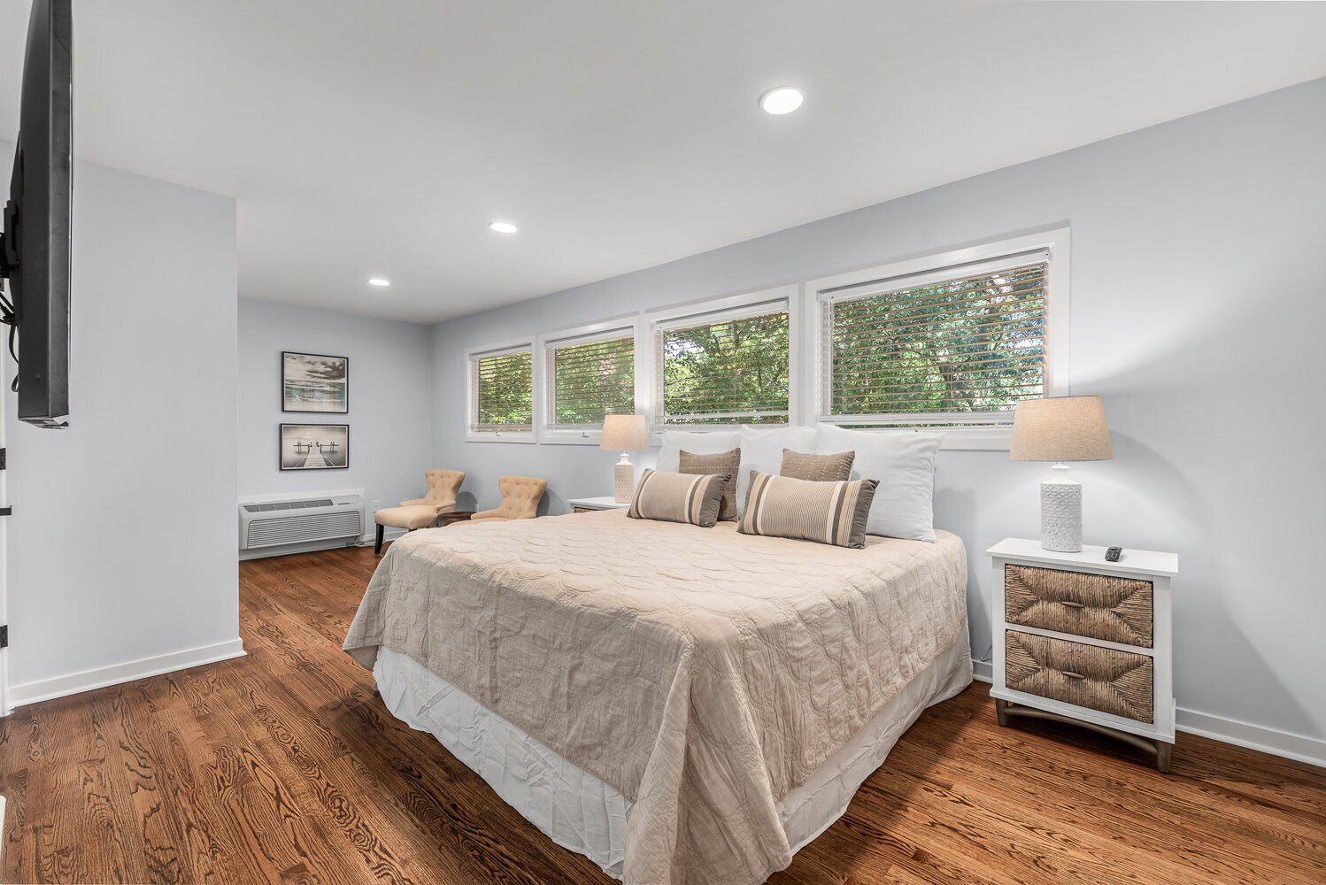 A bedroom with a large bed, two bedside tables, a nightstand, and a window with blinds.