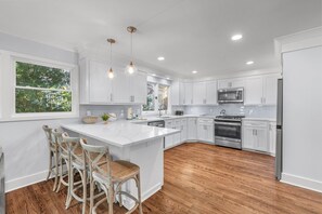 A modern kitchen with white cabinetry, a large island with bar stools, a stainless steel oven, and a microwave.