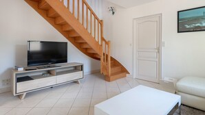 A living room with a wooden staircase, a flat-screen TV on a wooden TV stand, a white door, and a white sofa. - House for 8 - Pool - 950m from the sea (Saint-Gildas-de-Rhuys)