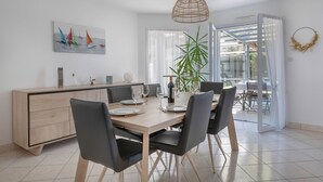 A modern dining area with a wooden table set for four, black chairs, a potted plant, and a painting of sailboats on the wall. - House for 8 - Pool - 950m from the sea (Saint-Gildas-de-Rhuys)