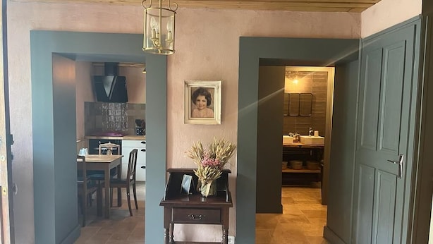 Un couloir avec un plafond en bois, un tableau encadré au mur et une table sur laquelle est posé un vase de fleurs.