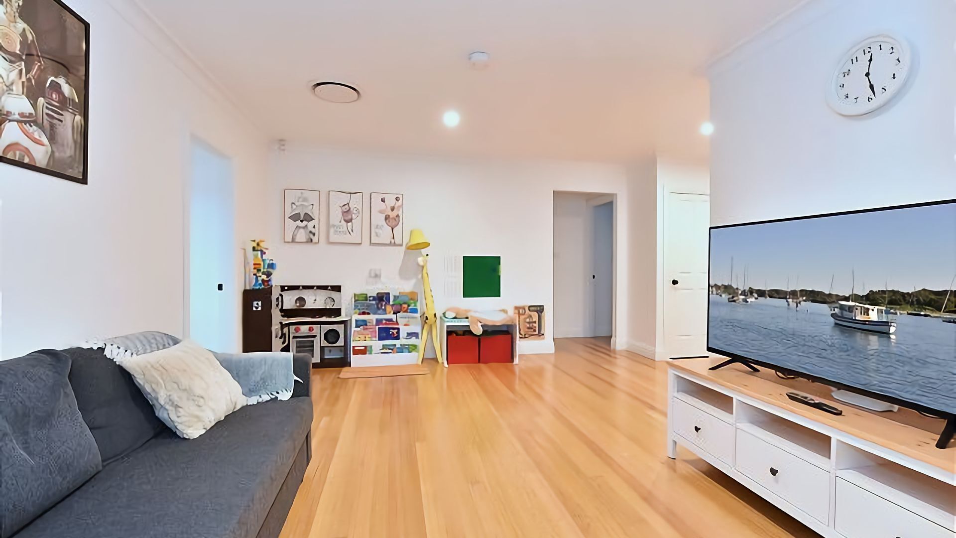 A modern living room with a sofa, TV, wooden flooring, and a children's play area.