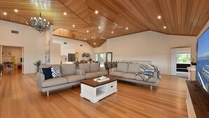 Un salon spacieux avec un plafond en bois, un grand ensemble de canapés, une table basse et un téléviseur.