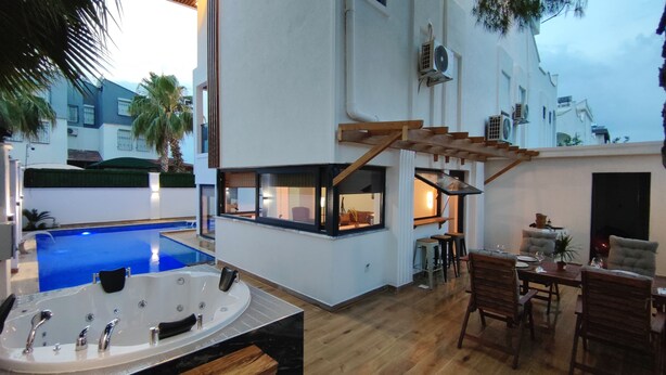 Et moderne poolområde med jacuzzi, træterrasse og siddeområde.