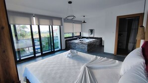 Et moderne soveværelse med en stor seng, et badeværelse med badekar og en balkon med udsigt til grønne områder.
