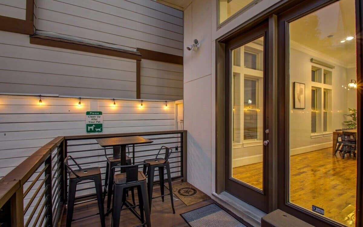 An outdoor patio with a wooden railing, a table, and chairs. There is a sign instructing to clean up after pets.