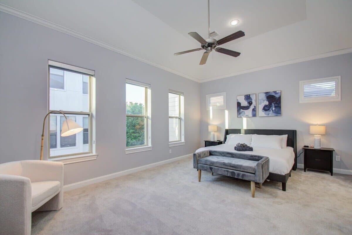 A bedroom with a bed, bedside tables, a ceiling fan, and large windows.