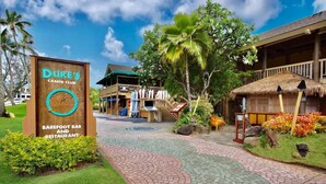 Duke's Sanctuary Club mit einer Bar und einem Restaurant ohne Schuhe, mit einem tropischen Garten, einer Struktur mit einem Reetdach und einem gepflasterten Weg.