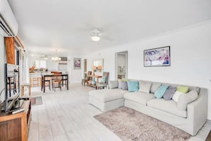 A modern living room with a sectional sofa, a dining area with a table and chairs, and a kitchen in the background.