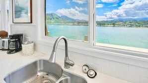 Eine Küche mit Spüle aus Edelstahl, einer Kaffeemaschine und einem Fenster mit Blick auf einen See und Berge.