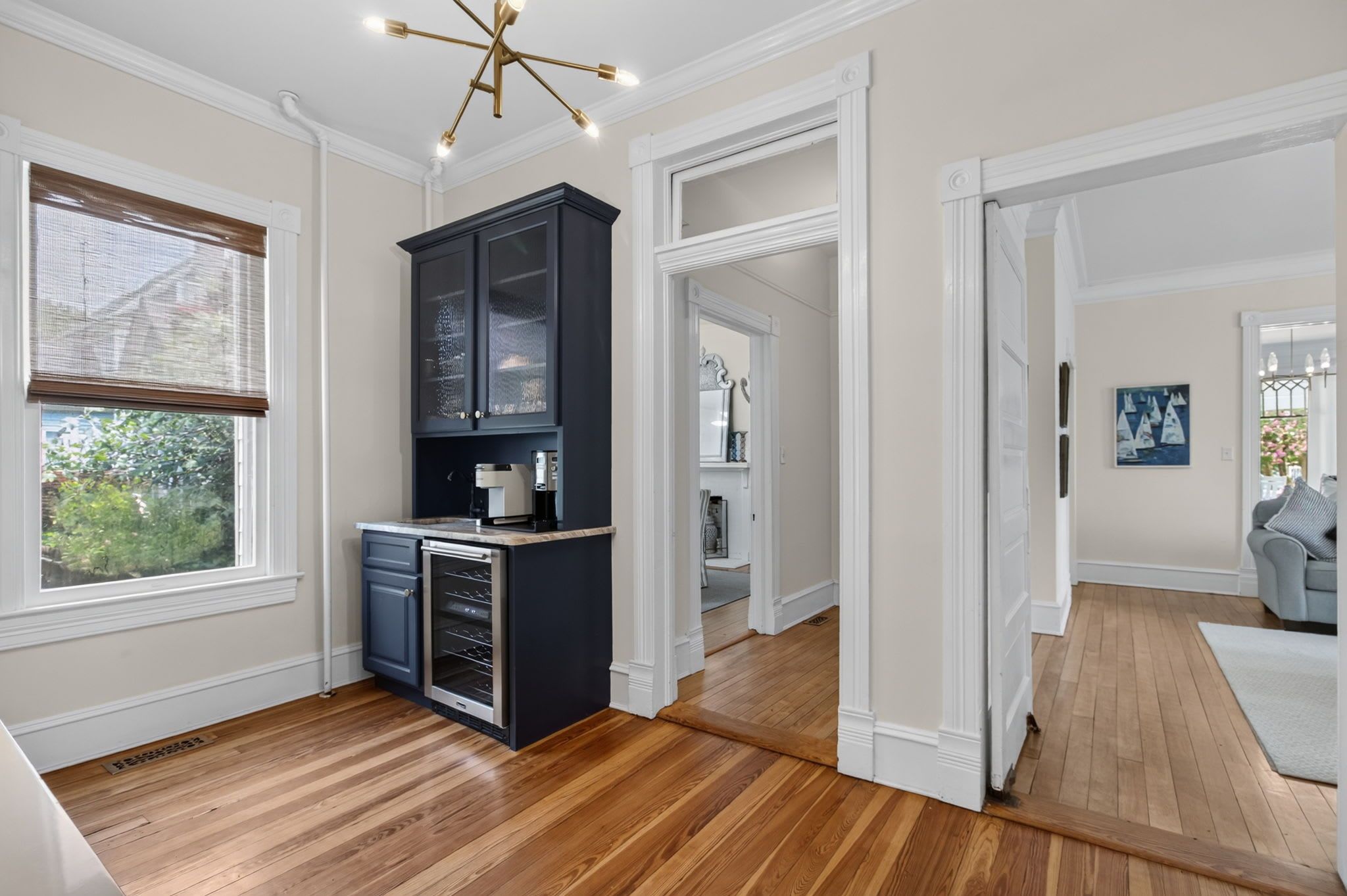 A kitchen with wooden flooring, a black cabinet, and a window with blinds.