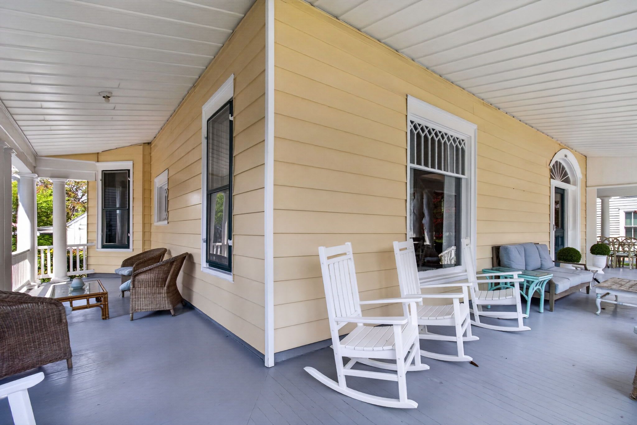 A covered porch with white rocking chairs, a glass coffee table, and a wicker sofa.