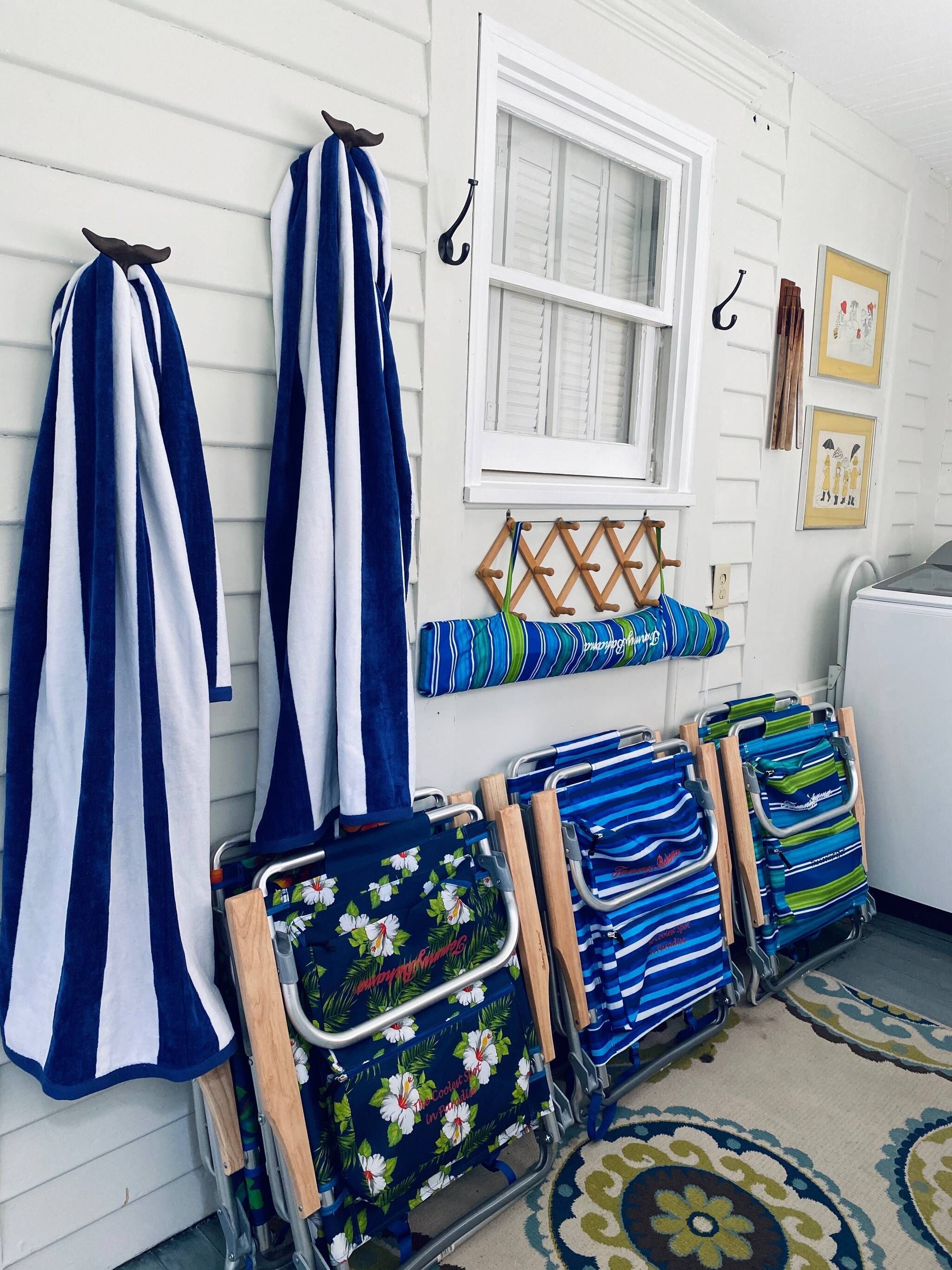 A room with striped towels hanging on hooks, a window with shutters, and a cart with folded towels.