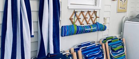 A room with striped towels hanging on hooks, a window with shutters, and a cart with folded towels.