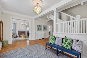 A spacious living room with a blue bench, a patterned rug, and a staircase with white railings.