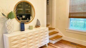 A hallway with a white console table, a round mirror, and a staircase. - Tazewell House Estate with Wraparound Porch (CAPE CHARLES)