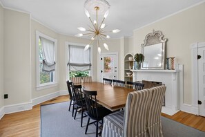 A dining room with a wooden table and chairs, a chandelier, and a fireplace with a mirror above it. - Tazewell House Estate with Wraparound Porch (CAPE CHARLES)