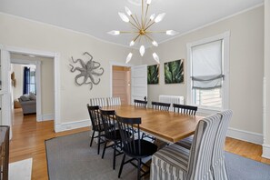 A dining area with a wooden table, black chairs, a patterned rug, and a modern chandelier. - Tazewell House Estate with Wraparound Porch (CAPE CHARLES)