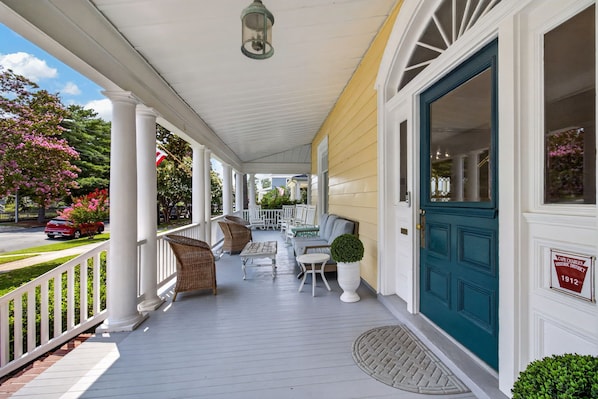A porch with white railings, wicker furniture, and a blue door.