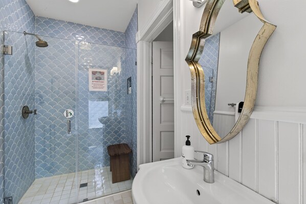 A bathroom with a glass shower enclosure, a white sink, and a large mirror with a gold frame.