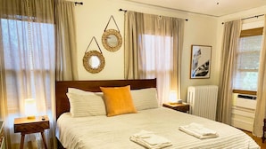 A neatly made bed with pillows, a bedside lamp, and a folded towel on a wooden floor. - Tazewell House Estate with Wraparound Porch (CAPE CHARLES)