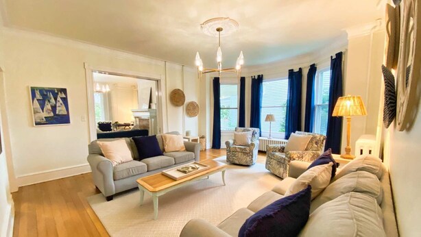 A living room with a sofa, armchairs, a coffee table, and a chandelier. - Tazewell House Estate with Wraparound Porch (CAPE CHARLES)