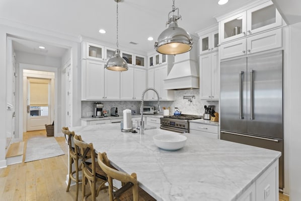 A modern kitchen with white cabinets, a large island, stainless steel appliances, and pendant lighting.