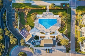 An aerial view of a hotel with a central swimming pool, a parking area, and landscaped gardens.