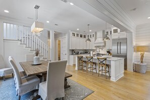 A spacious kitchen with white cabinetry, a central island with bar stools, and a modern pendant light fixture.
