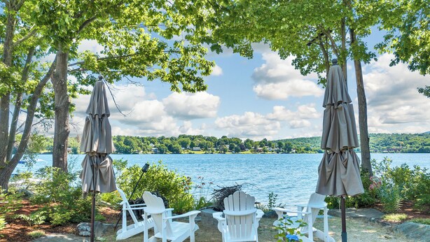 Un espacio de descanso junto al lago con sillas Adirondack y sombrillas, con vistas a un lago tranquilo.