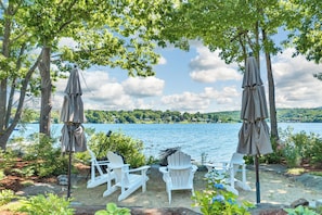 A lakeside seating area with Adirondack chairs and umbrellas, overlooking a calm lake. - Modern Lake Opechee Home features Sandy Perched Beach and Dock (Laconia)