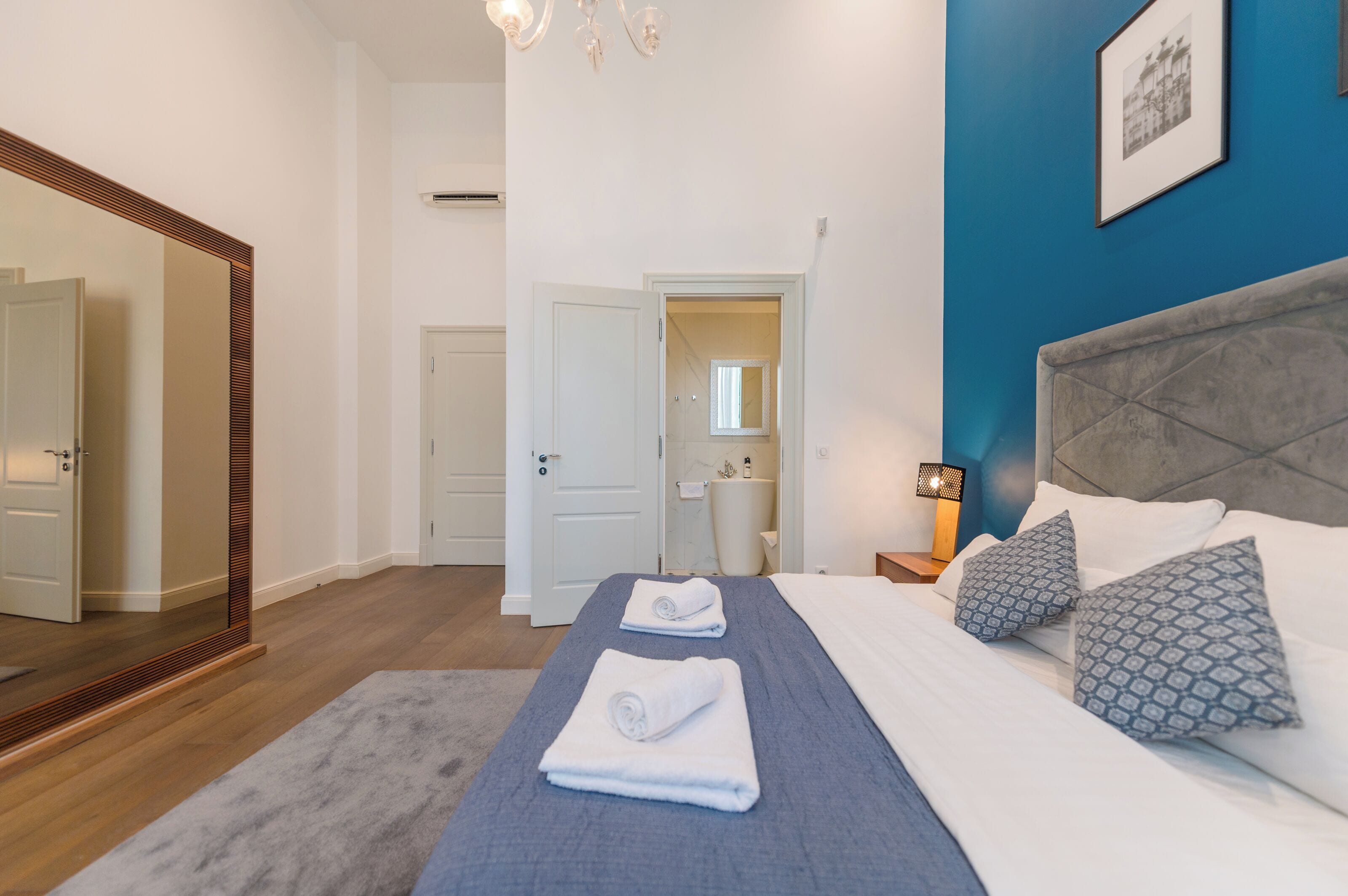 A hotel room with a large bed, a mirror, a door, and a bathroom visible through an open door.