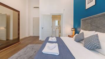 Habitación de hotel con una cama grande, un espejo, una puerta y un baño visible a través de una puerta abierta.