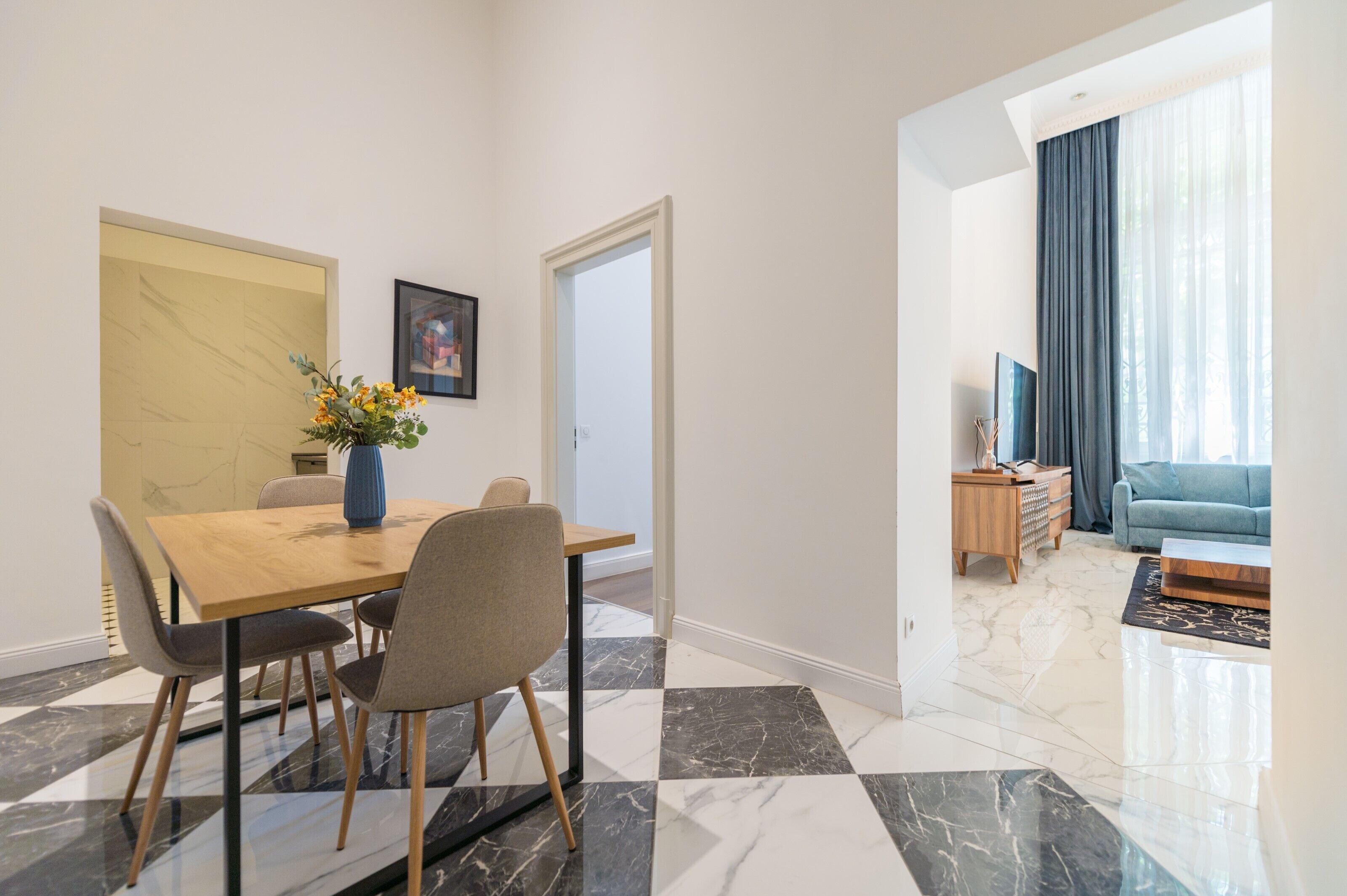 A modern dining area with a wooden table and chairs, a vase with flowers, and a marble floor.