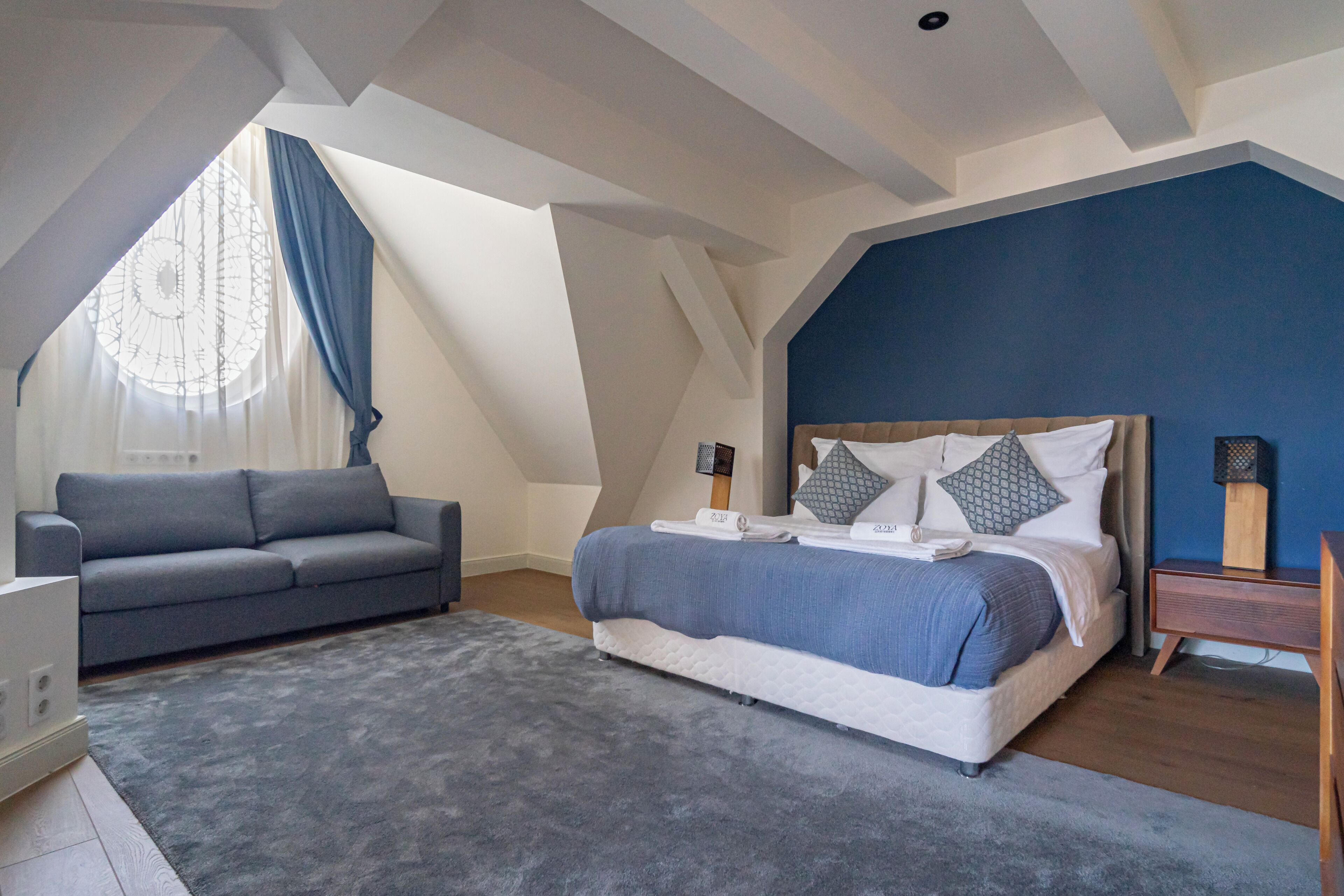 A bedroom with a bed, a sofa, a nightstand, and a window with curtains.