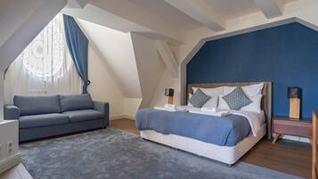 A bedroom with a bed, a sofa, a nightstand, and a window with curtains.