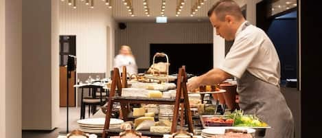 Montaje de buffet con diversas estaciones de comida señalizadas, una encimera de mármol y lámparas colgantes.