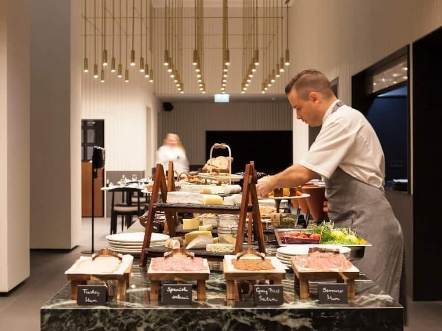 A buffet setup with various food stations labeled, a marble countertop, and hanging pendant lights.