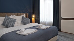 A neatly made bed with blue bedding and patterned pillows, a bedside lamp, and a view of a window with curtains. - ZOYA LUXURY RESIDENCE (Budapest)