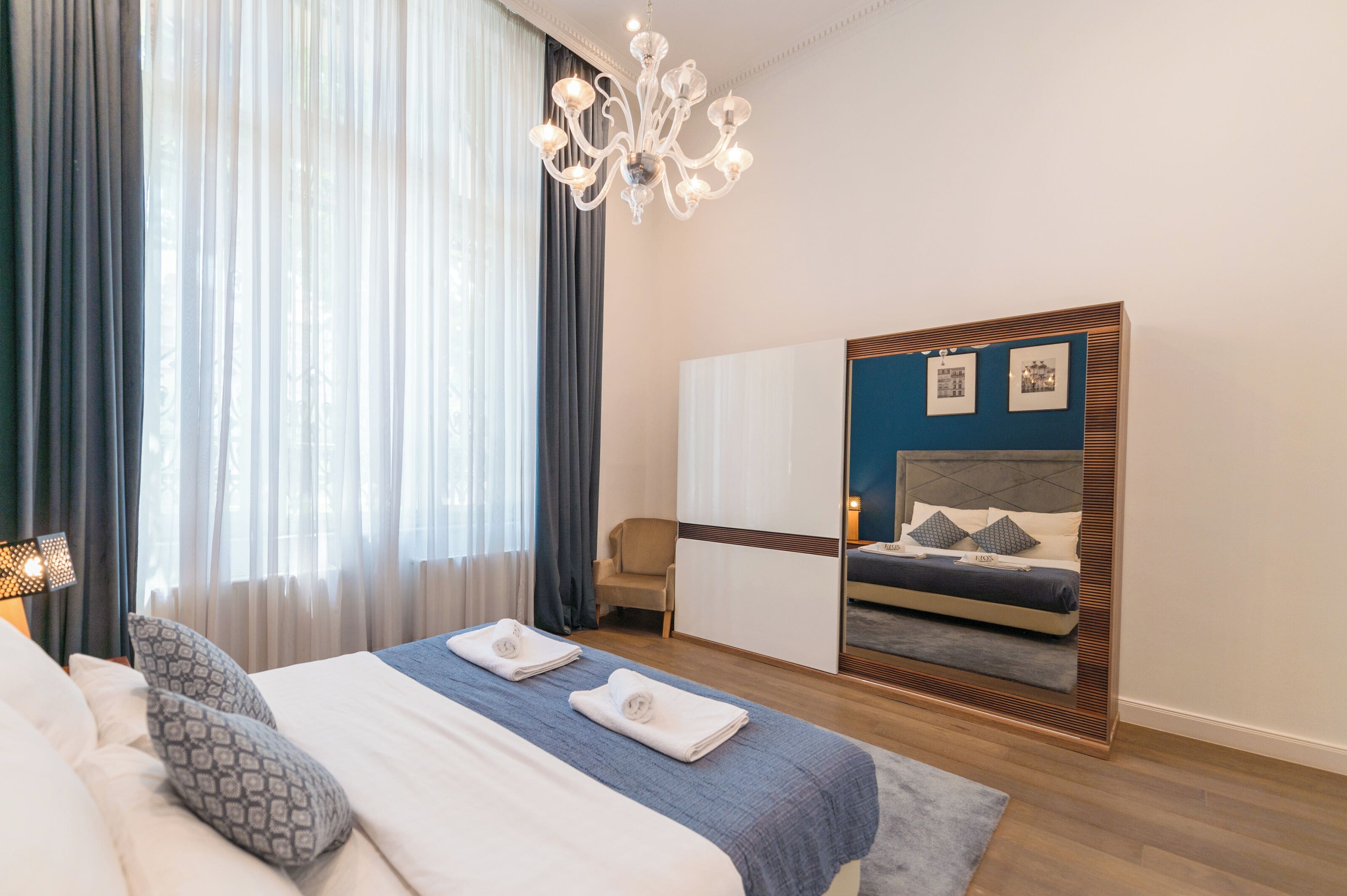 A hotel room with a large bed, a wardrobe, a mirror, and a chandelier.