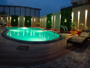 A swimming pool with a wooden deck, surrounded by potted plants and a covered seating area. - Surasena Regalvista (Agra)