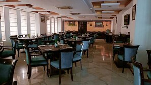 A spacious restaurant with multiple dining tables and chairs, large windows, and a modern ceiling design. - Surasena Regalvista (Agra)